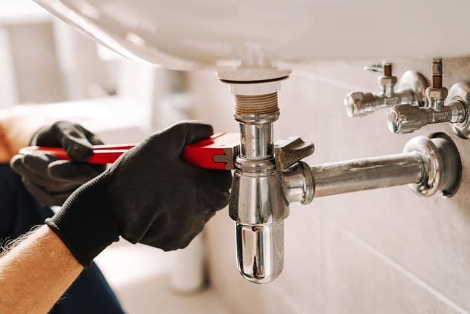 Plumber repairing a sink pipe with an adjustable wrench